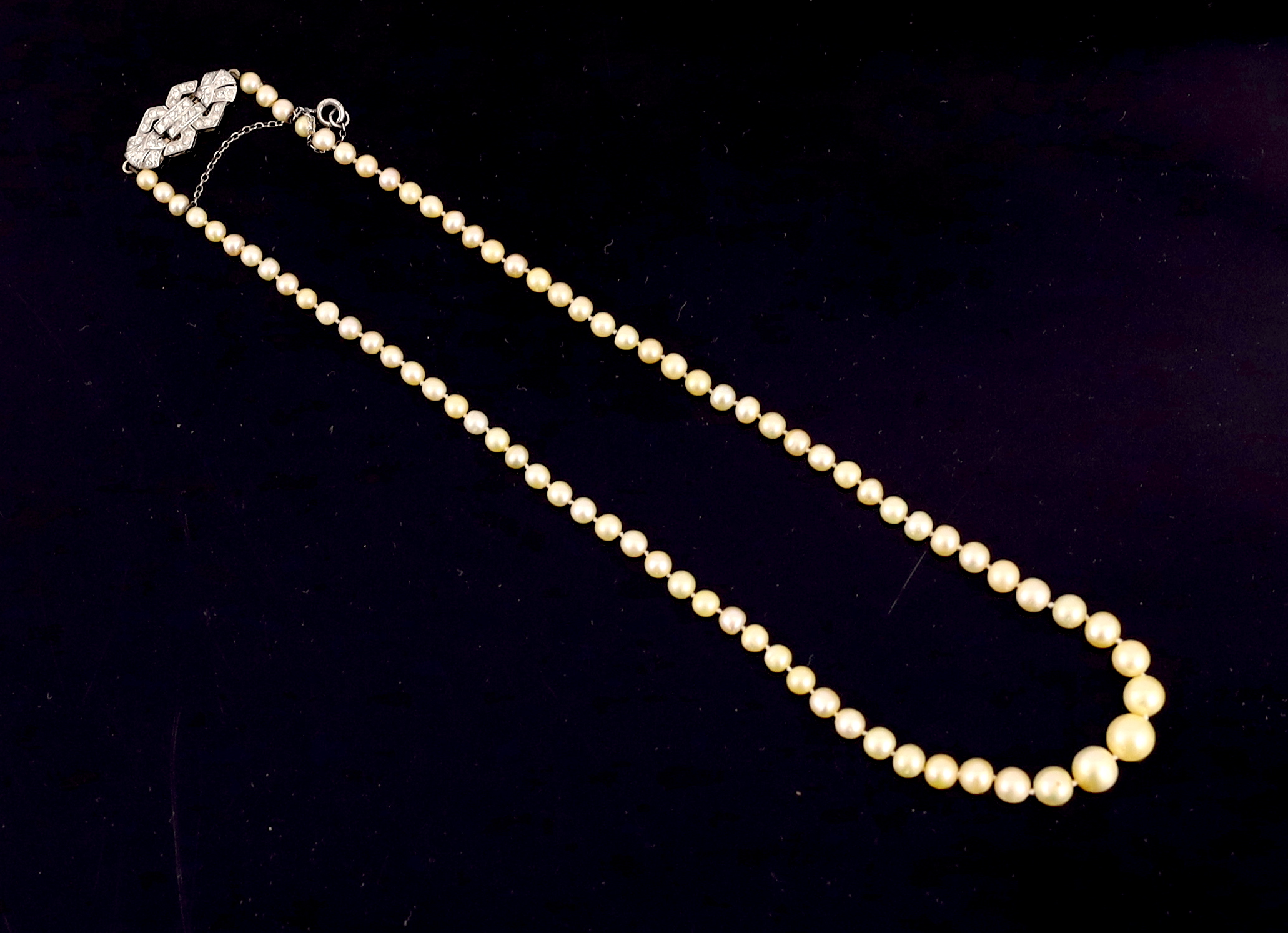 An Edwardian single strand graduated natural saltwater pearl necklace, with gold, platinum and diamond cluster set clasp, with safety chain